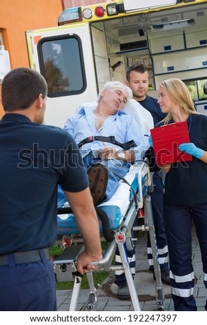 Paramedical team helping injured senior man lying on stretcher outdoors