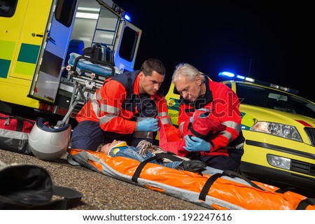 Paramedics giving first-aid to injured motorbike woman driver at night