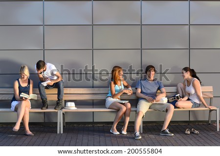 College students sitting on bench by modern wall outside campus