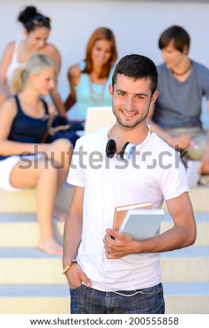 Smiling student boy  holding books friends sitting on college steps