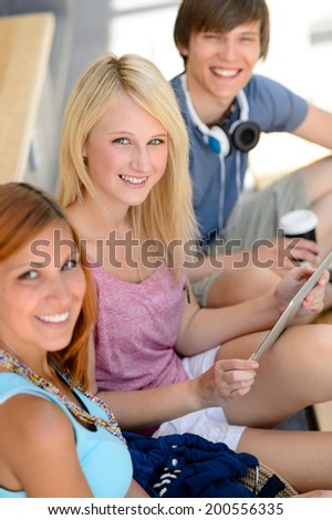 Three student friends sitting with tablet smiling at camera