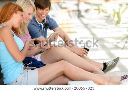 Cheerful college student friends using tablet together sitting in assembly hall