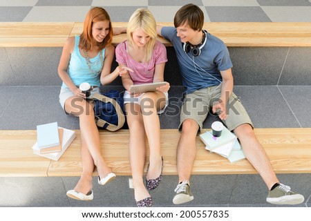 Three college student friends with tablet and books sitting