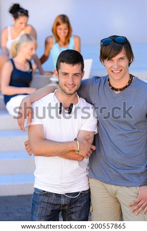 Two student boys standing outside college girl friends in background