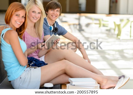 Three college student friends with tablet smiling looking at camera