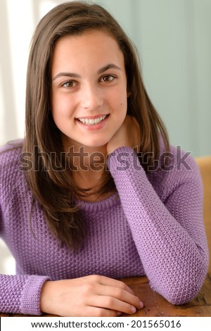 Cute teenage girl sitting behind table wear purple jumper portrait
