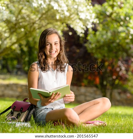 Cheerful girl with open book sitting on grass summer park