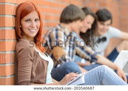 Young student woman sitting outside college friends in background