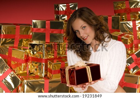 Beautiful brunette offering a Christmas gift in front of pile of gifts
