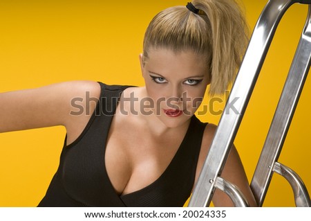 Blond girl leaning on aluminum ladder on yellow background