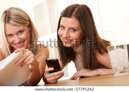 Two smiling students enjoying free time with book and mobile phone