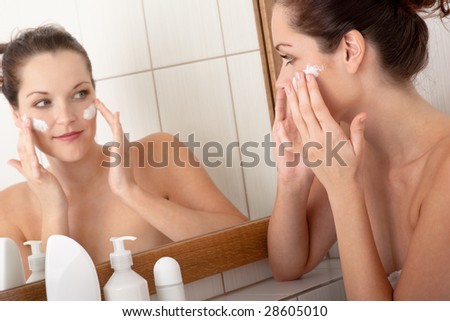 Body care series - Beautiful young woman applying cream in the bathroom