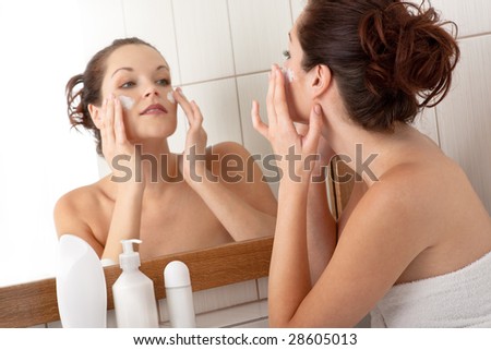 Body care series - Beautiful young woman applying cream in the bathroom