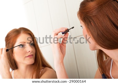 Body care - Beautiful young woman applying mascara in front of mirror