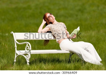 Red hair woman reading book on white bench in a meadow in spring