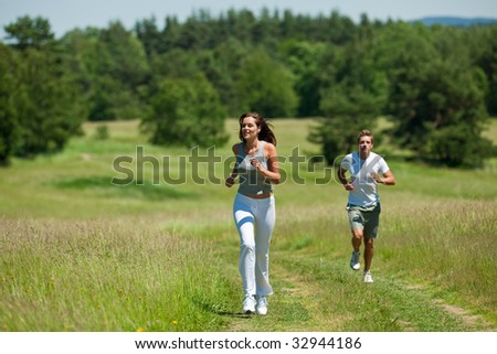 Young woman with headphones jogging, man in background, shallow DOF