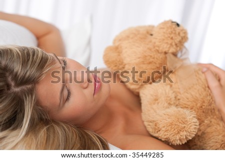 Portrait of beautiful woman holding teddy bear lying on white bed