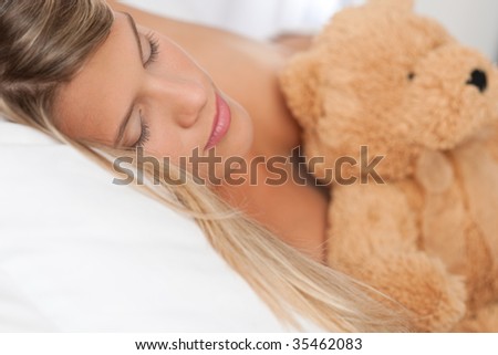 Sleeping woman holding brown teddy bear on white bed