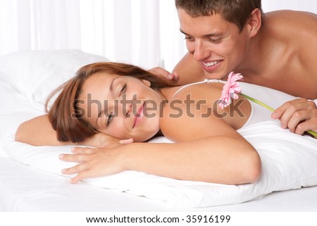 Happy man and woman lying down in bed together, man holding Gerber daisy