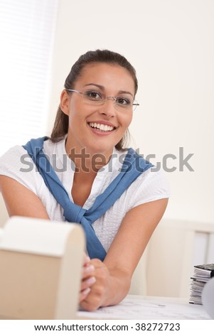 Happy female architect with architectural model sitting at the office