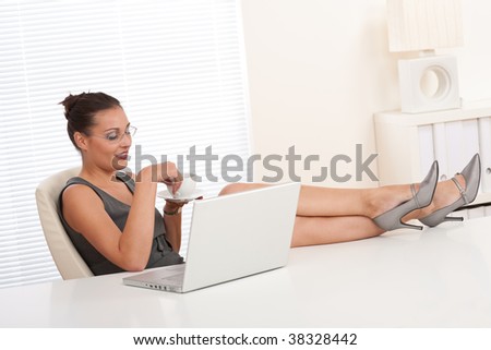 Attractive businesswoman having coffee and feet on table at the office