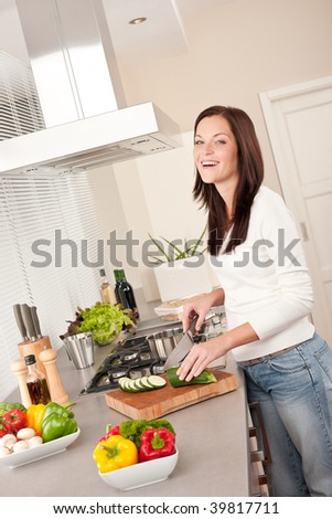 Smiling happy woman cutting zucchini in the kitchen and cooking