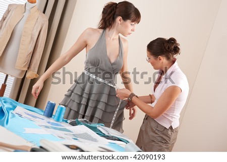 Female fashion designer measuring model for fitting gray dress, taking measurement