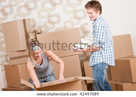 New house: Young couple with box in new home unpacking book