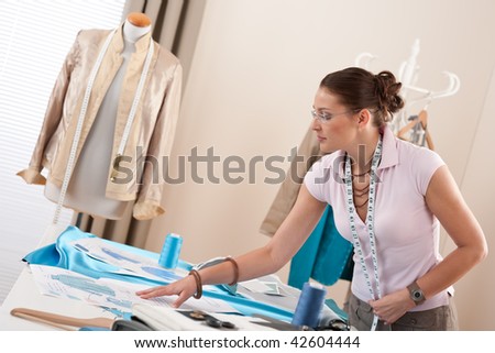 Female fashion designer working at studio with pattern cuttings and sketches
