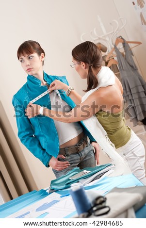 Female fashion designer measuring turquoise jacket on model, taking measurements