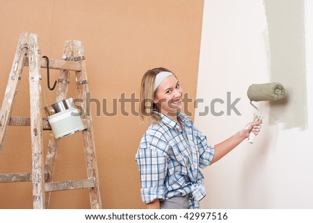 Home improvement: Happy woman painting wall with paint roller
