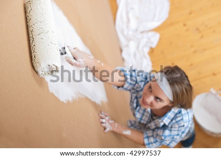 Home improvement: Young woman painting wall with paint roller