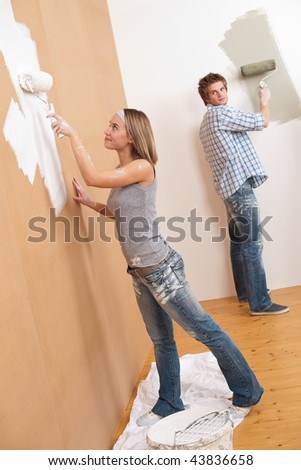 Home improvement: Young couple painting wall with paint roller