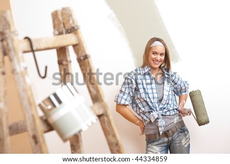 Home improvement: Young woman with paint roller and ladder painting wall