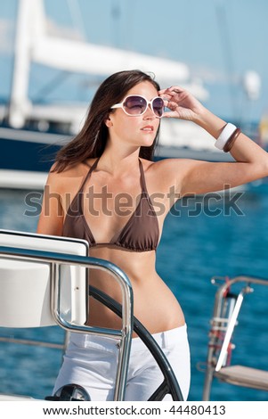 Beautiful young woman standing on luxury boat holding rudder