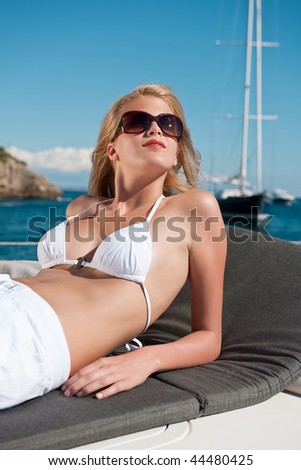 Blond woman sunbathing on luxury yacht with bikini and sunglasses