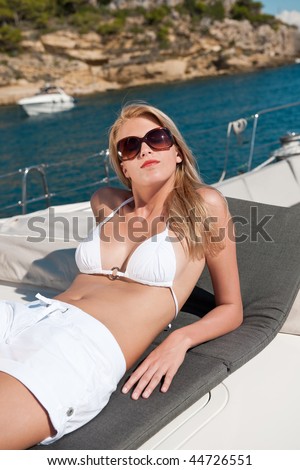 Blond woman sunbathing on luxury yacht with bikini and sunglasses