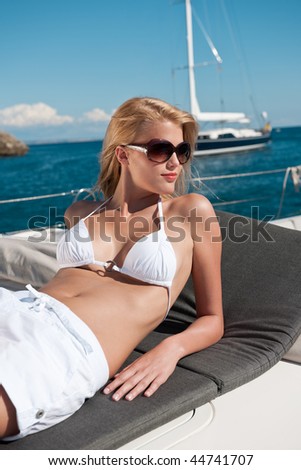 Blond woman sunbathing in white bikini on luxury yacht on the sea