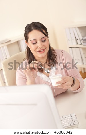 Young businesswoman eating yogurt at office, having break