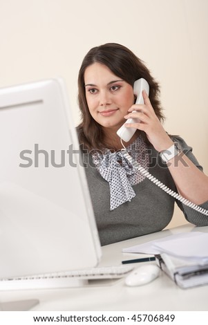 Attractive executive woman on phone at office watching computer screen