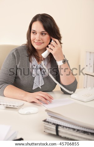 Smiling secretary on phone at modern office sitting at desk