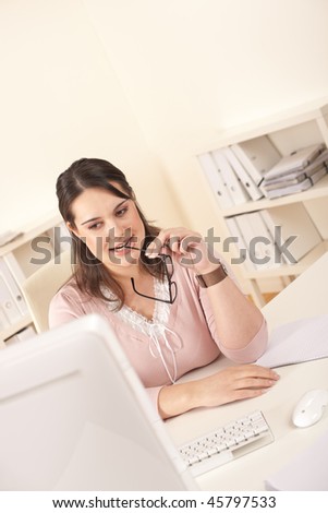 Young businesswoman watching computer screen thinking and holding glasses
