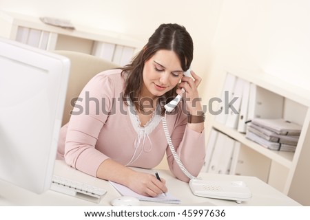 Young secretary on phone at modern office in front of computer