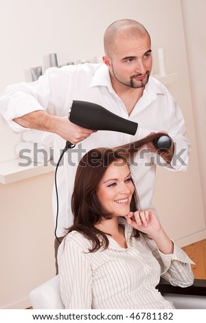 Professional male hairdresser with hair dryer at salon with female customer