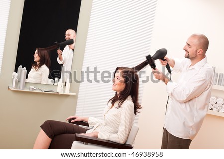 Professional male hairdresser with hair dryer and hair brush at salon with female customer