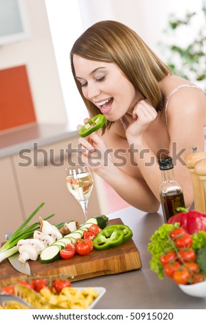 Cooking - happy woman biting slice of green pepper in modern kitchen