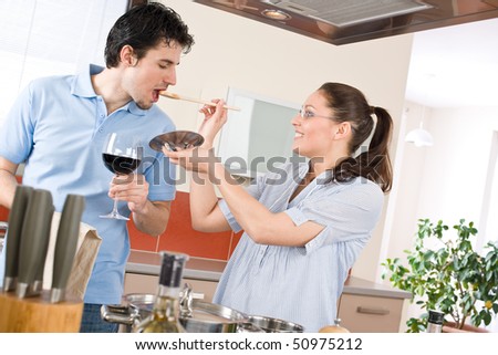 Happy couple cook together in modern kitchen tasting food, drink red wine
