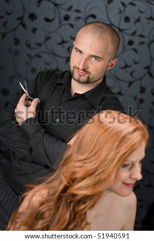 Professional hairdresser with long red curly hair fashion model at black luxury salon, hair cut with scissors