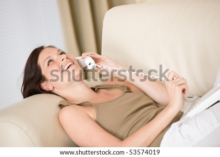 On the phone home: Smiling woman lying down on sofa calling watching up