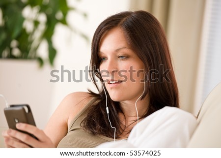 Woman holding music player listening with earbuds home, plant in background